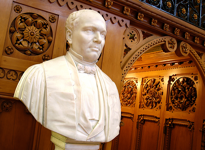A sculpted white marble bust of Sir Étienne-Paschal Taché in front of a sculpted wooden-paneled wall